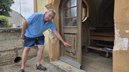 Bild: Tobias Gräf
Kapellen-Kümmerer Norbert Eisner zeigt, wie hoch das Wasser in und vor der Kirche stand. Das kleine Rohr neben seinem linken Bein ist zu klein, um bei Starkregen Wasser schnell genug abfließen zu lassen.