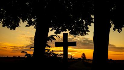 Bild: Moritz Frankenberg/dpa
Der Himmel hinter einem Kreuz strahlt kurz vor Sonnenaufgang orange. Friedhöfe sind für viele Angehörige ein besonderer Ort der Trauer.