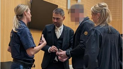 Bild: wüw
Vor Beginn des sechsten Verhandlungstags löst eine Vorführbeamte den Angeklagten im Müllprozess die Handschellen. Die Verteidiger Stefanie Amann und Rouven Colbatz hätten gerne, dass der 53-Jährige dem Prozess künftig dauerhaft ohne Fesseln folgen kann.