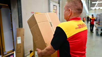 Bild: Sebastian Christoph Gollnow/dpa
Ein Paketbote schleppt in einem DHL-Standort ein schweres Paket. (Archivbild)