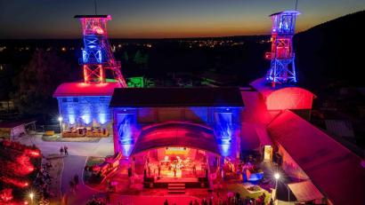 Bild: Michel Grüner / Förderverein Maffeispiele
Das Classic-Rock-Festival G:O:A findet auf dem Gelände des Bergbaumuseums Maffeischächte statt. Neben der Bühnenbeleuchtung werden in der Dämmerung auch die Fördertürme illuminiert.