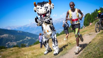 Bild: Maxime Schmid/KEYSTONE/dpa
Philemon Ombogo Kiriago beim 53. Sierre-Zinal-Berglauf: Fan in Kuh-Kostüm sorgt für tierische Unterstützung