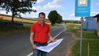 Bild: Josef Rosner
Bürgermeister Andreas Malzer mit den Plänen zur Wasserleitungserneuerung in Groppenheim, im Hintergrund die Kreisstraße TIR 15 in Richtung Münchenreuth, die ab Montag, 17. August, komplett gesperrt sein wird.