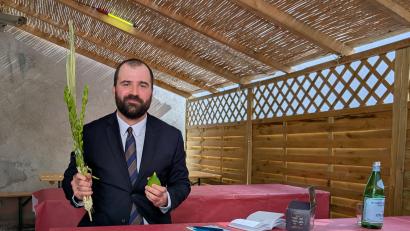 Bild: wüw
Florian Speil sitzt hier nicht einfach in einer Gartenlaube. Es ist ein Sukka, eine Laubhütte, die während des jüdischen Fest Sukot eine wichtige Rolle spielt. Sie darf nur vorübergehend und nur aus organischen Stoffen gebaut werden. In der Hand hält Speil Palmwedel und Früchte, denn Sukot ist auch ein Erntedankfest.