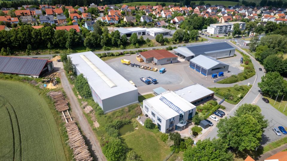 Die Drohnenaufnahme zeigt das Firmengelände der Firma Pöllath am Kreinzlweg in Erbendorf. Im Vordergrund befinden sich das Verwaltungs- und Ausstellungsgebäude, dahinter die Lagerhallen, Garagenflächen sowie die neue Werkstatt. Von dort aus werden jährlich rund 9.000 Baustelleneinsätze koordiniert. Bild: Roland Wellenhöfer